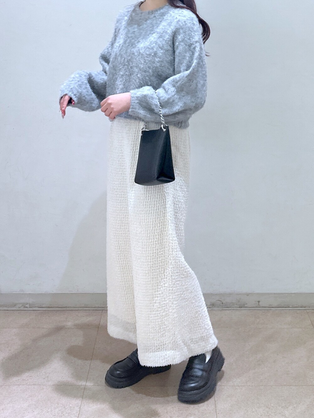 グレー系のニット/セーター、ブラック系のショルダーバッグ、ホワイト系のスカートを着用したレディースの冬コーディネートの3枚目の写真