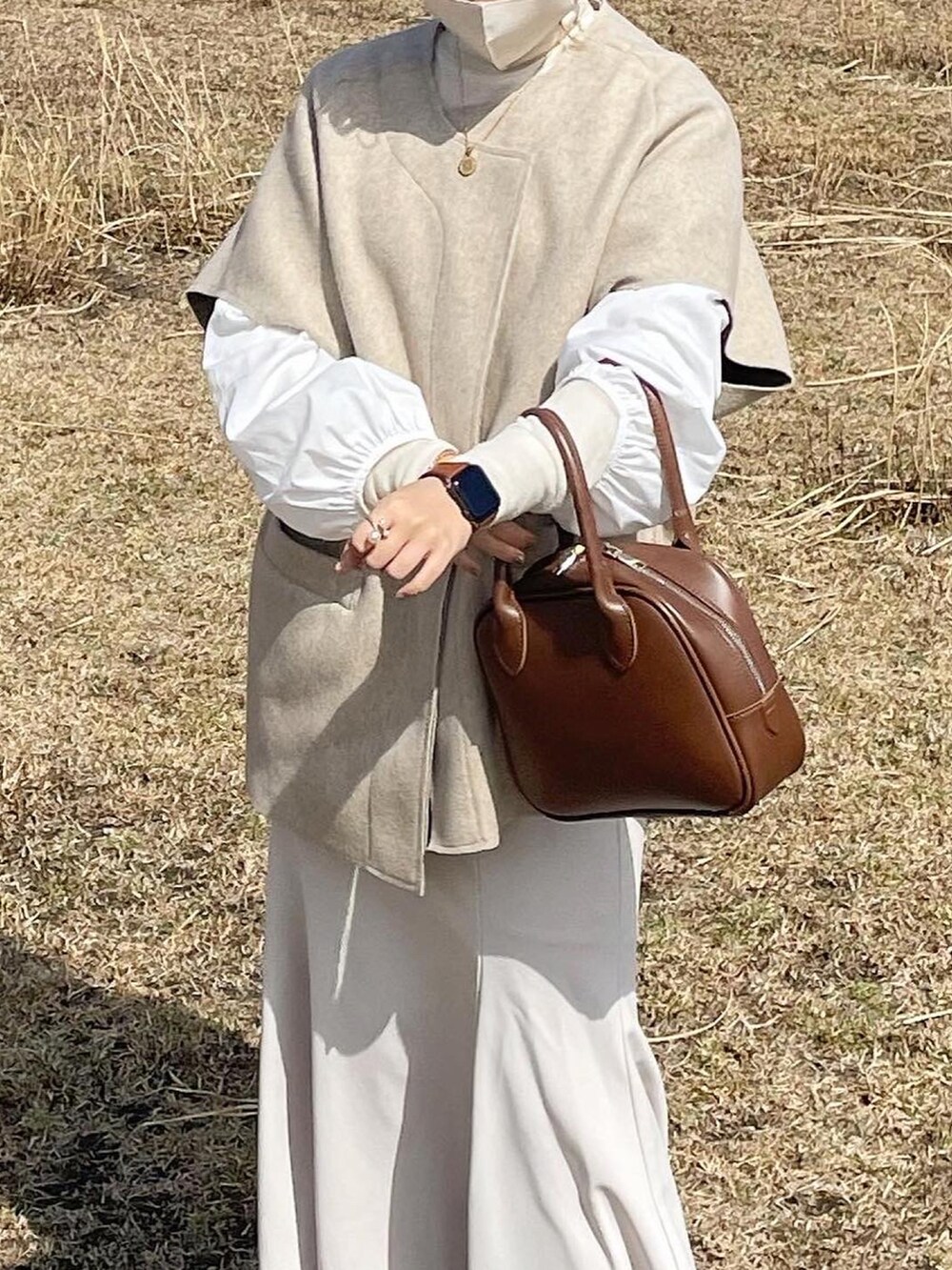 ブラウン系のショルダーバッグ、ブラウン系のブーツ、ホワイト系のスカートを着用したレディースの春コーディネートの2枚目の写真