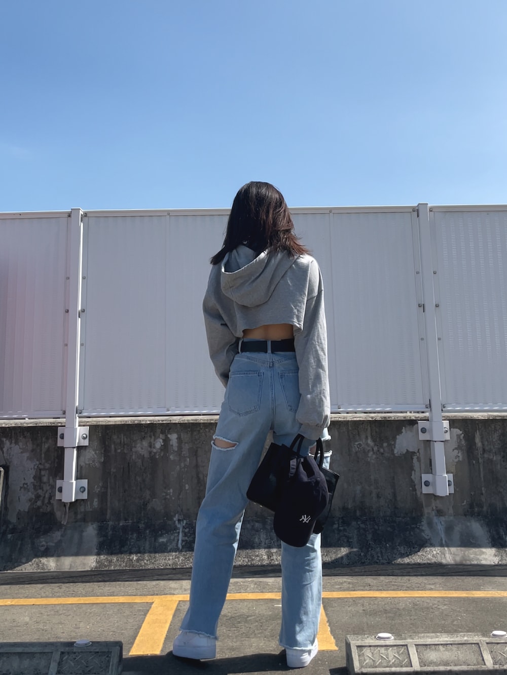 ブルー系のデニムパンツ、ブラック系のバッグ、ホワイト系のスニーカーを着用したレディースの夏コーディネートの2枚目の写真