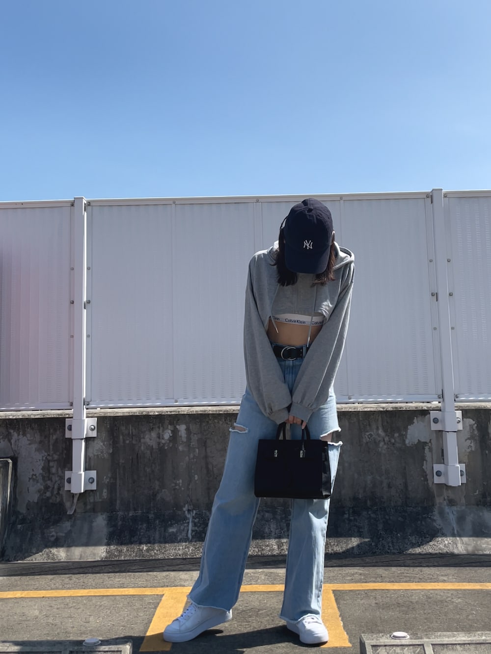 ブルー系のデニムパンツ、ブラック系のバッグ、ホワイト系のスニーカーを着用したレディースの夏コーディネートの3枚目の写真