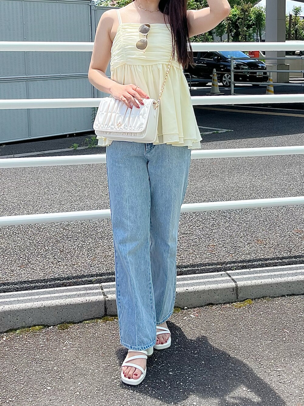イエロー系のキャミソール、ホワイト系のショルダーバッグ、ブルー系のデニムパンツを着用したレディースの夏コーディネートの3枚目の写真