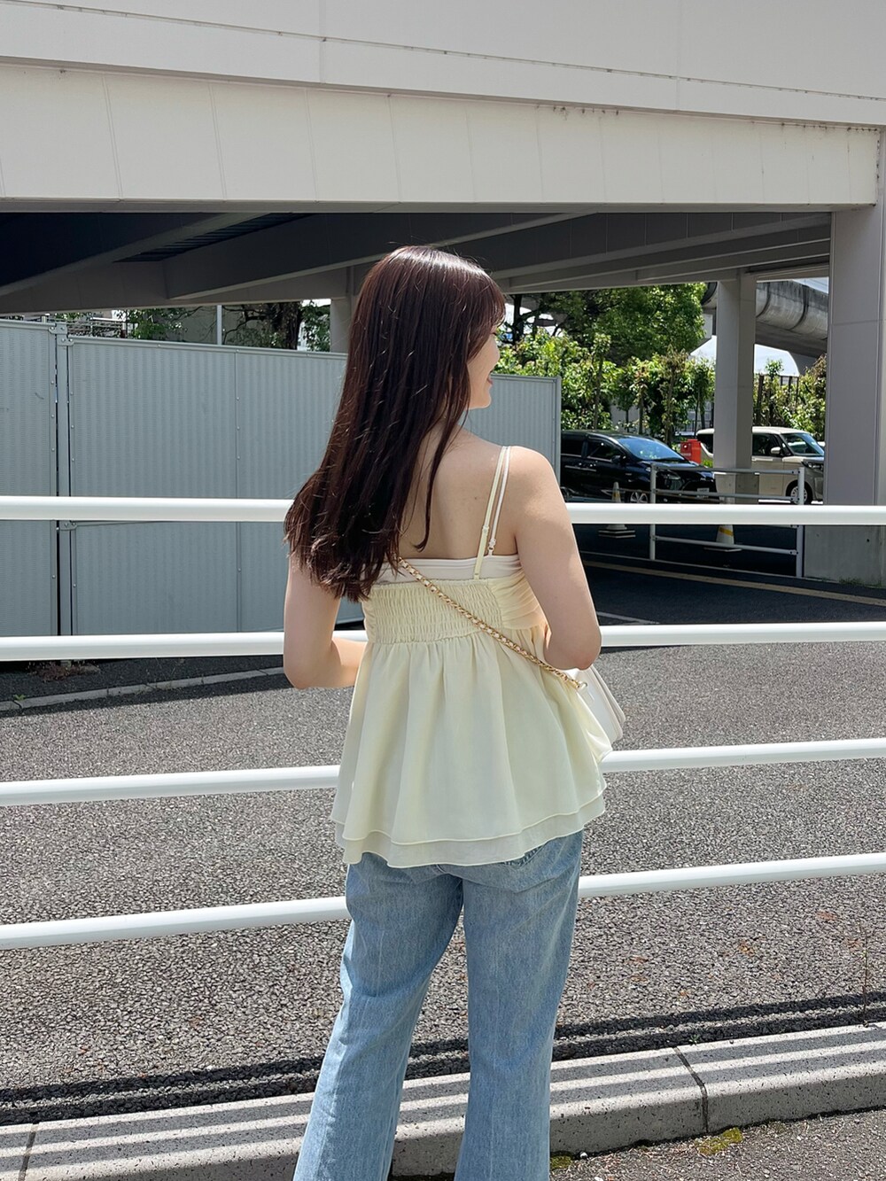 イエロー系のキャミソール、ホワイト系のショルダーバッグ、ブルー系のデニムパンツを着用したレディースの夏コーディネートの2枚目の写真