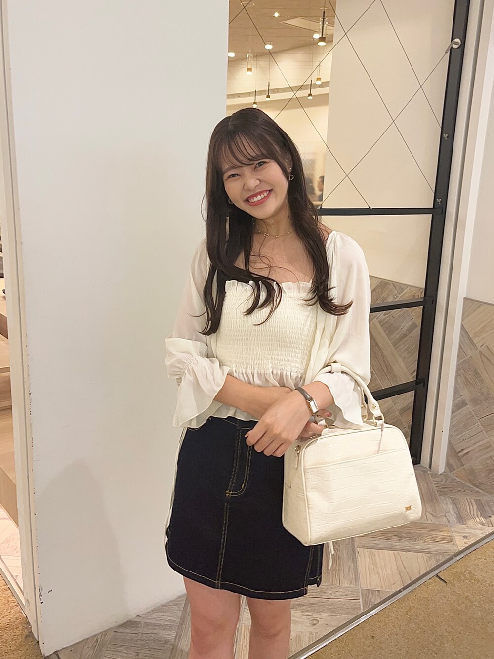 ホワイト系のシャツ/ブラウス、ホワイト系のボストンバッグ、ブルー系のデニムスカートを着用したレディースの夏コーディネートの2枚目の写真