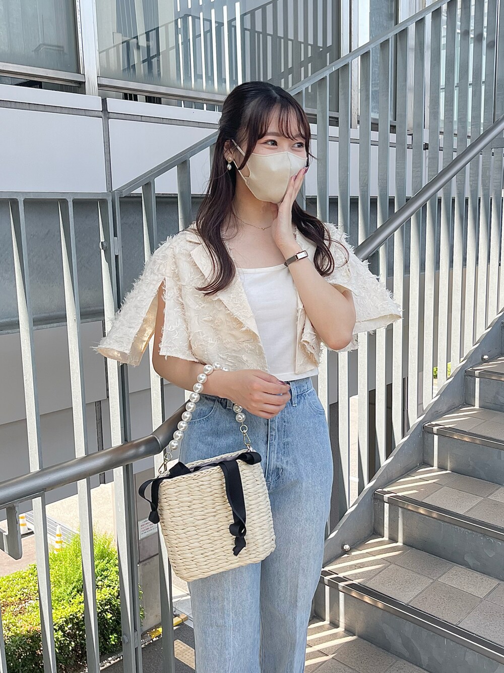 ブルー系のデニムパンツ、ブラック系のかごバッグ、ホワイト系のキャミソールを着用したレディースの春コーディネートの2枚目の写真