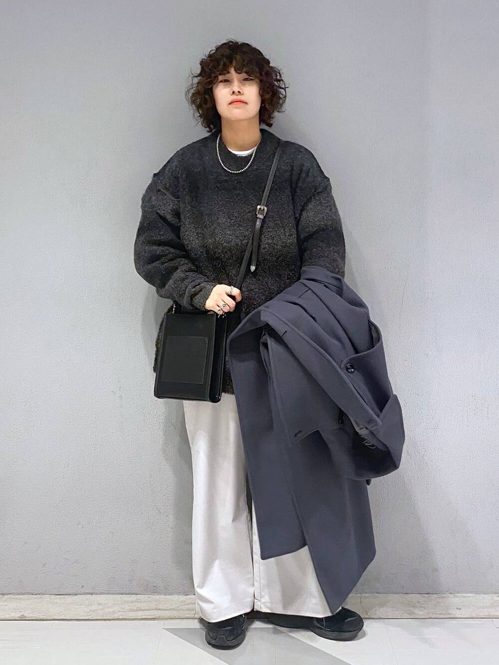 グレー系のトレンチコート、ブラック系のニット/セーター、ブラック系のショルダーバッグを着用したメンズの冬コーディネートの7枚目の写真