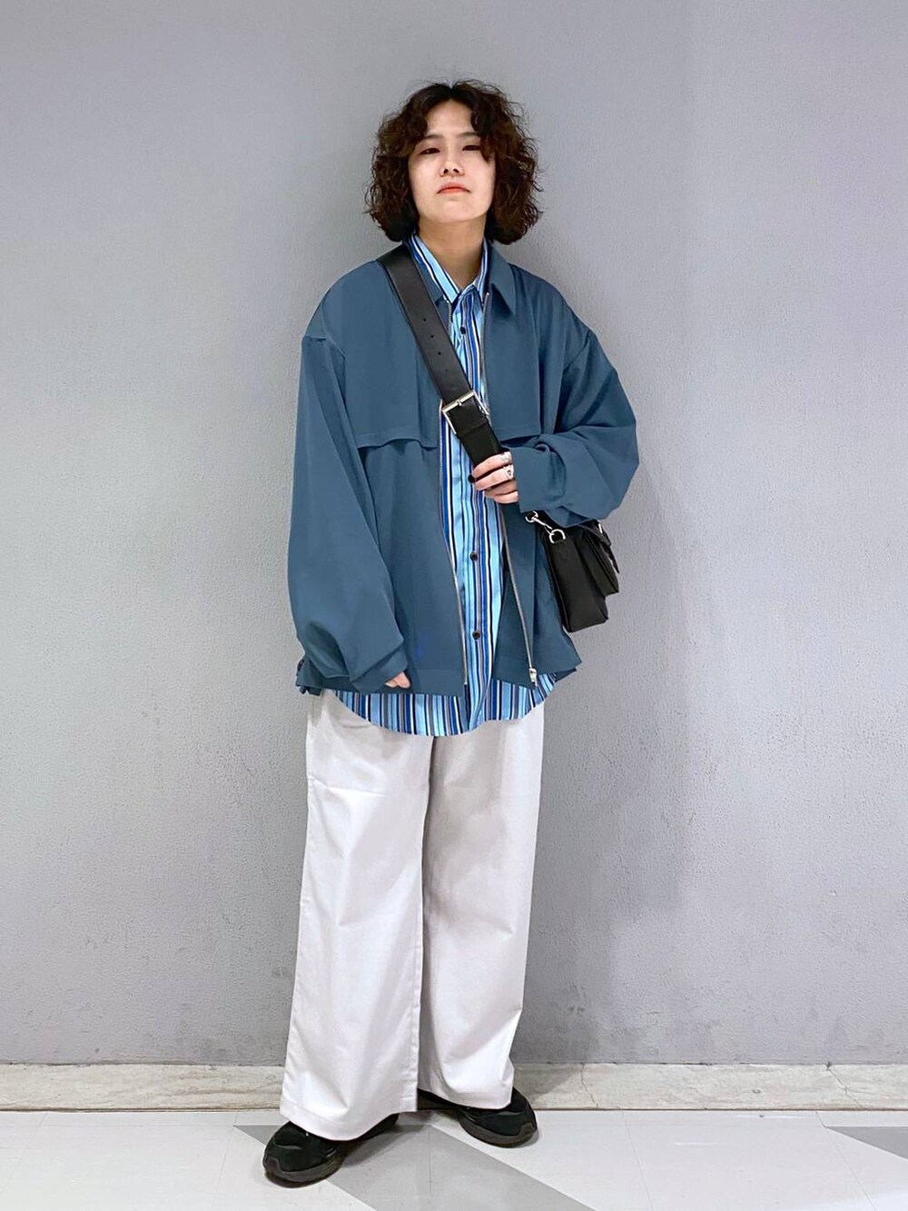 ブラック系のショルダーバッグ、ホワイト系のスラックス、ブルー系のブルゾンを着用したメンズの春コーディネートの2枚目の写真