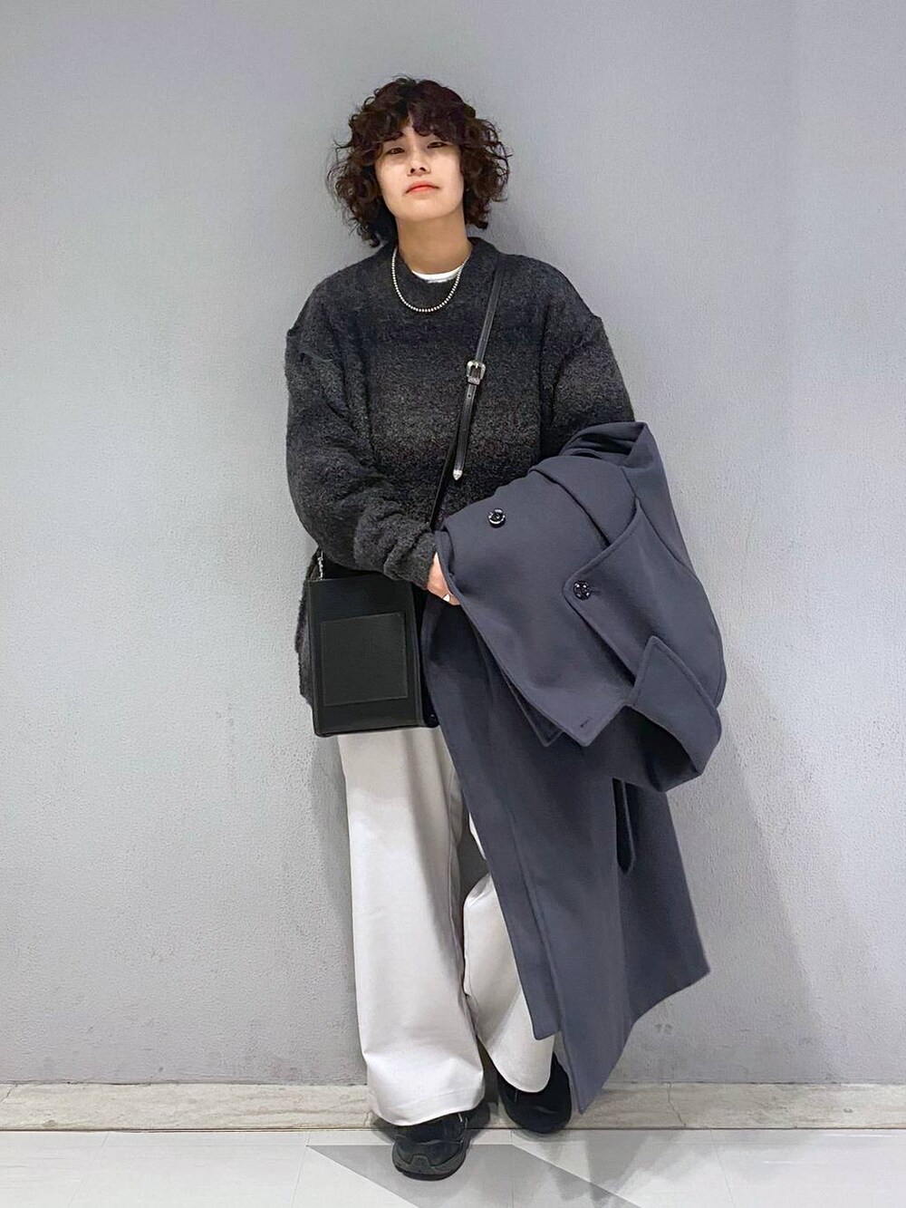 グレー系のトレンチコート、ブラック系のニット/セーター、ブラック系のショルダーバッグを着用したメンズの冬コーディネートの6枚目の写真