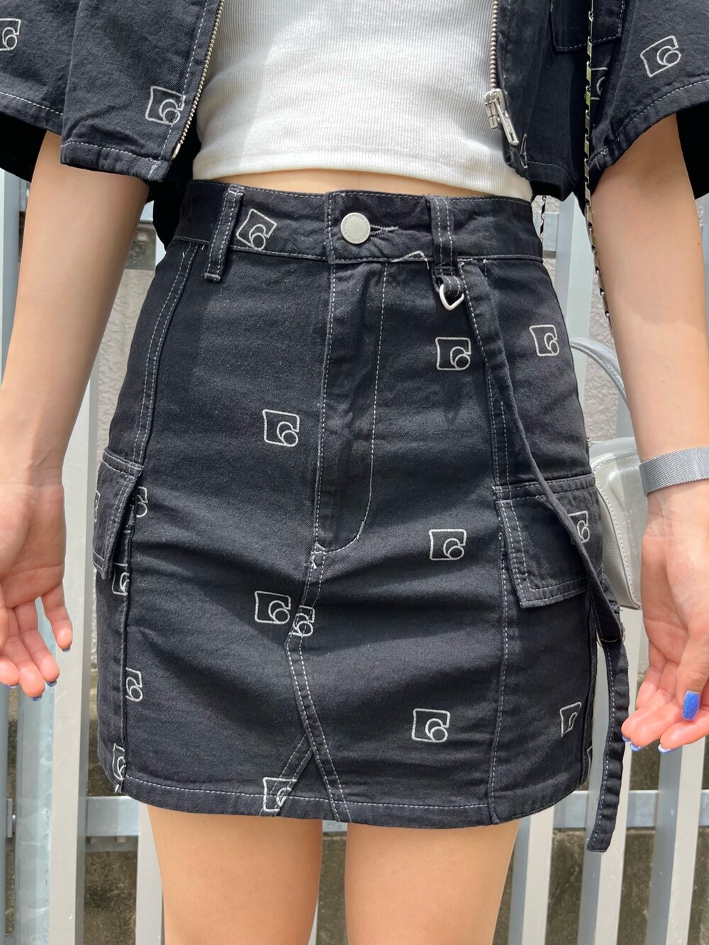 シルバー系のハンドバッグ、ブラック系のデニムスカート、ホワイト系のキャミソールを着用したレディースの夏コーディネートの6枚目の写真