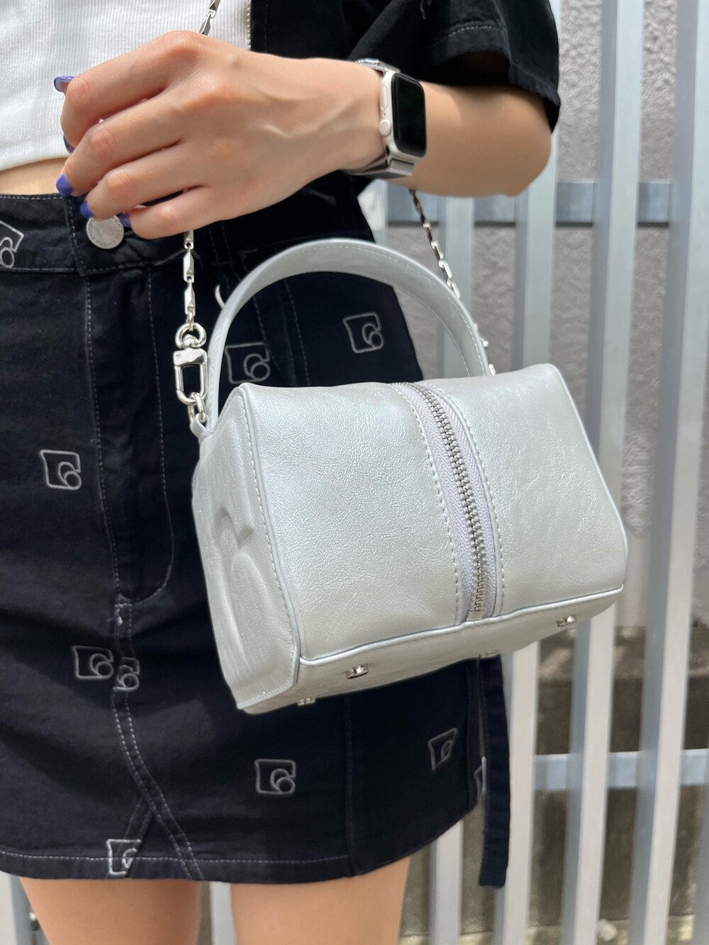 シルバー系のハンドバッグ、ブラック系のデニムスカート、ホワイト系のキャミソールを着用したレディースの夏コーディネートの8枚目の写真