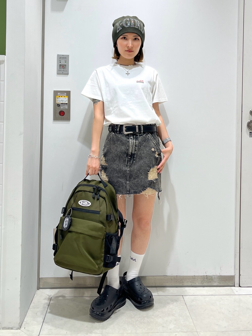 ブラック系のデニムスカート、グリーン系のバックパック/リュック、ホワイト系のTシャツ/カットソーを着用したレディースの夏コーディネートの2枚目の写真