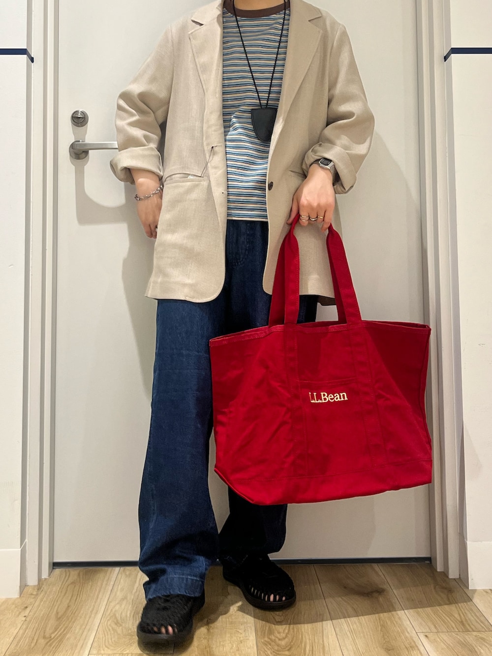 ブラック系のサンダル、ブルー系のデニムパンツ、レッド系のトートバッグを着用したレディースの春コーディネートの6枚目の写真