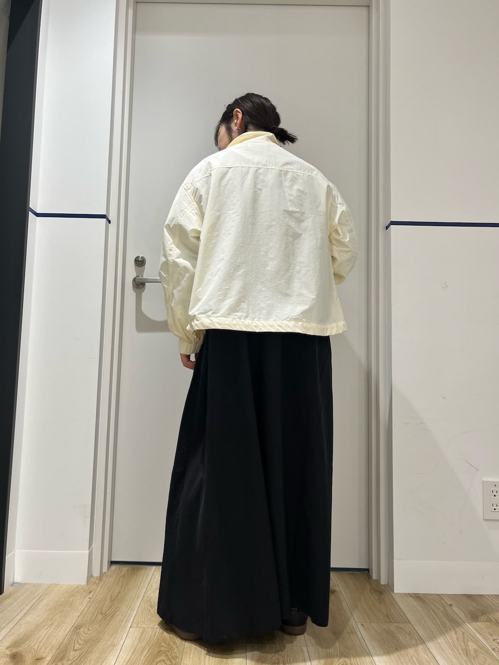 ブラック系のワンピース、ブラック系のスニーカー、ホワイト系のナイロンジャケットを着用したレディースの春コーディネートの3枚目の写真