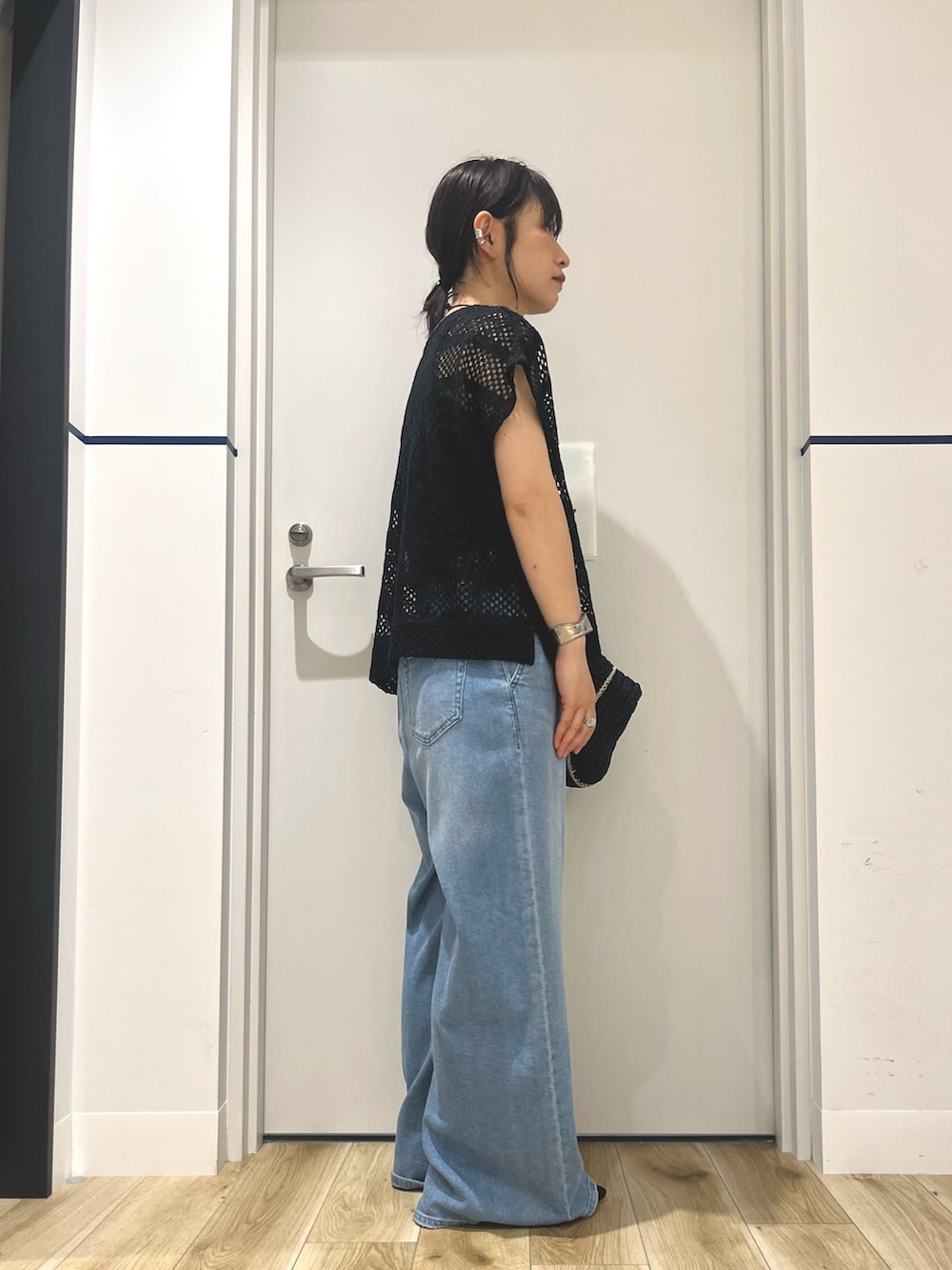 ブラック系のニット/セーター、ブラック系のトートバッグ、ブルー系のデニムパンツを着用したレディースの夏コーディネートの2枚目の写真