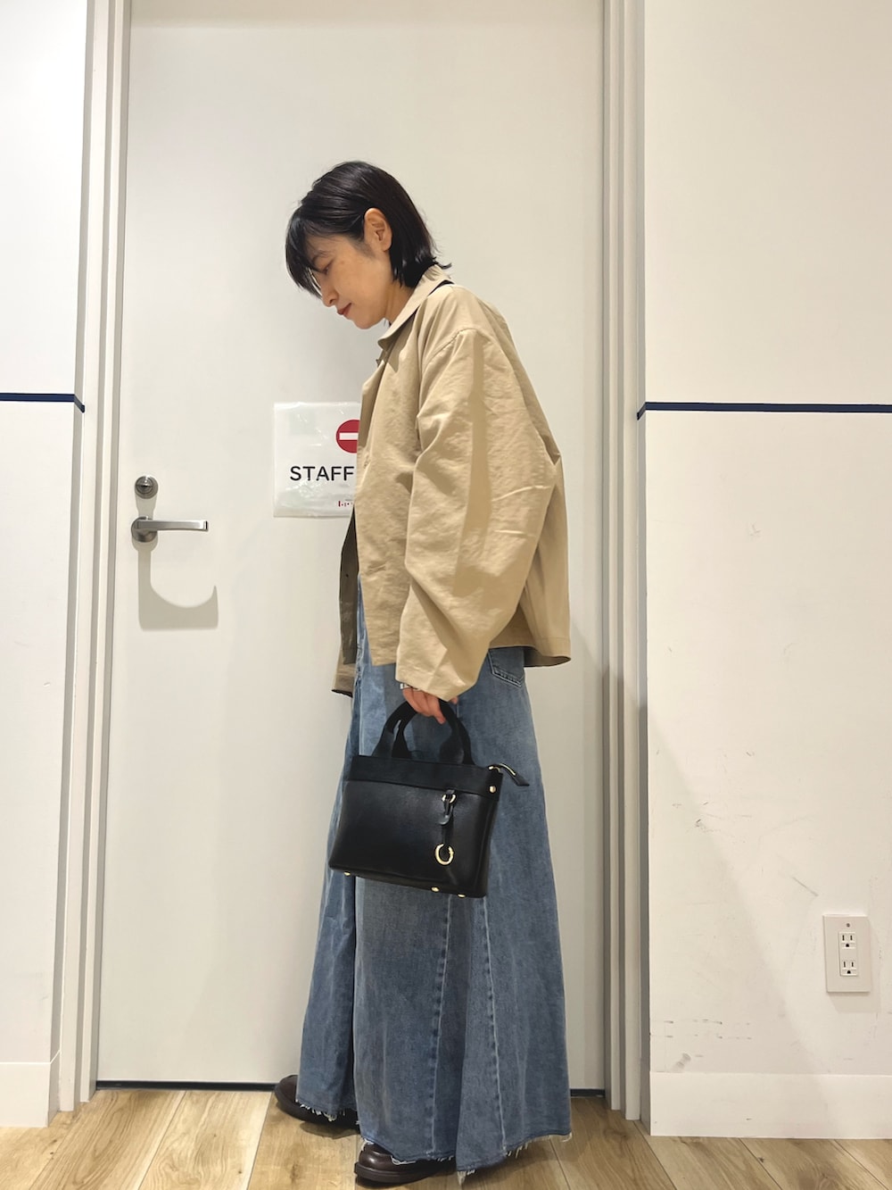 ブラウン系のローファー、ブルー系のスカート、ブラック系のハンドバッグを着用したレディースの秋コーディネートの2枚目の写真
