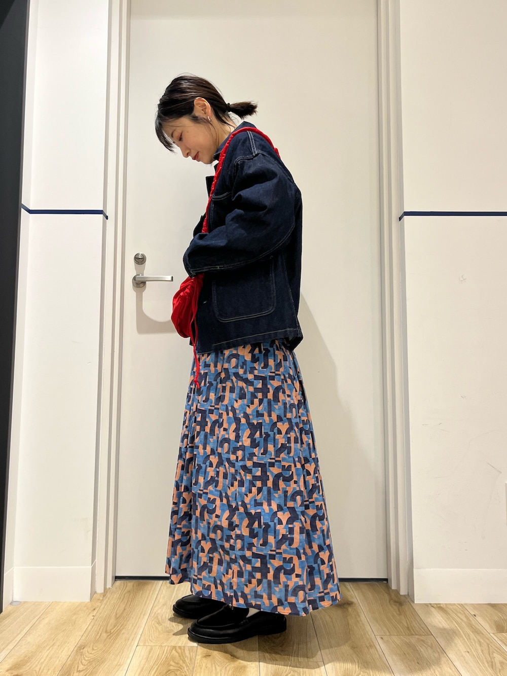 ブラック系のローファー、ブルー系のスカート、レッド系のショルダーバッグを着用したレディースの春コーディネートの2枚目の写真