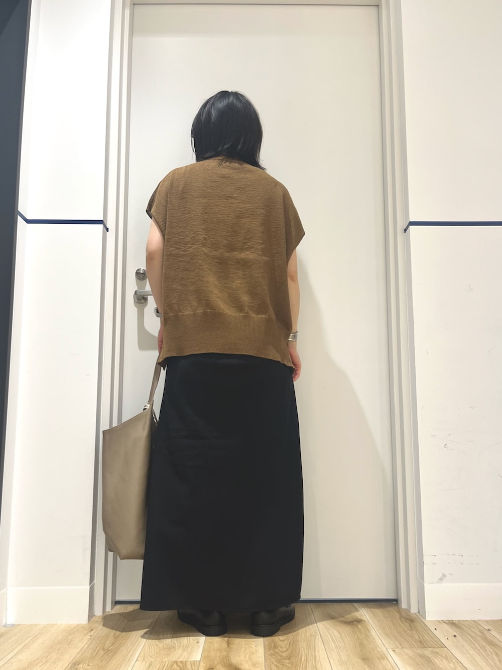 ブラック系のスカート、ブラウン系のベスト、ベージュ系のトートバッグを着用したレディースの夏コーディネートの2枚目の写真