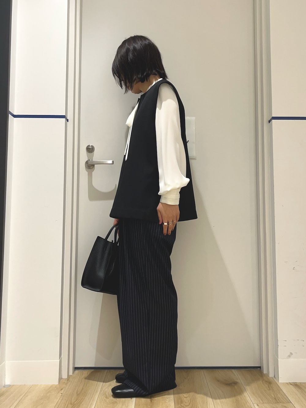 ホワイト系のシャツ/ブラウス、ブラック系のベスト、ブラック系のハンドバッグを着用したレディースの秋コーディネートの2枚目の写真