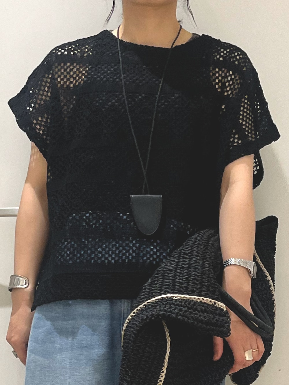 ブラック系のニット/セーター、ブラック系のトートバッグ、ブルー系のデニムパンツを着用したレディースの夏コーディネートの3枚目の写真