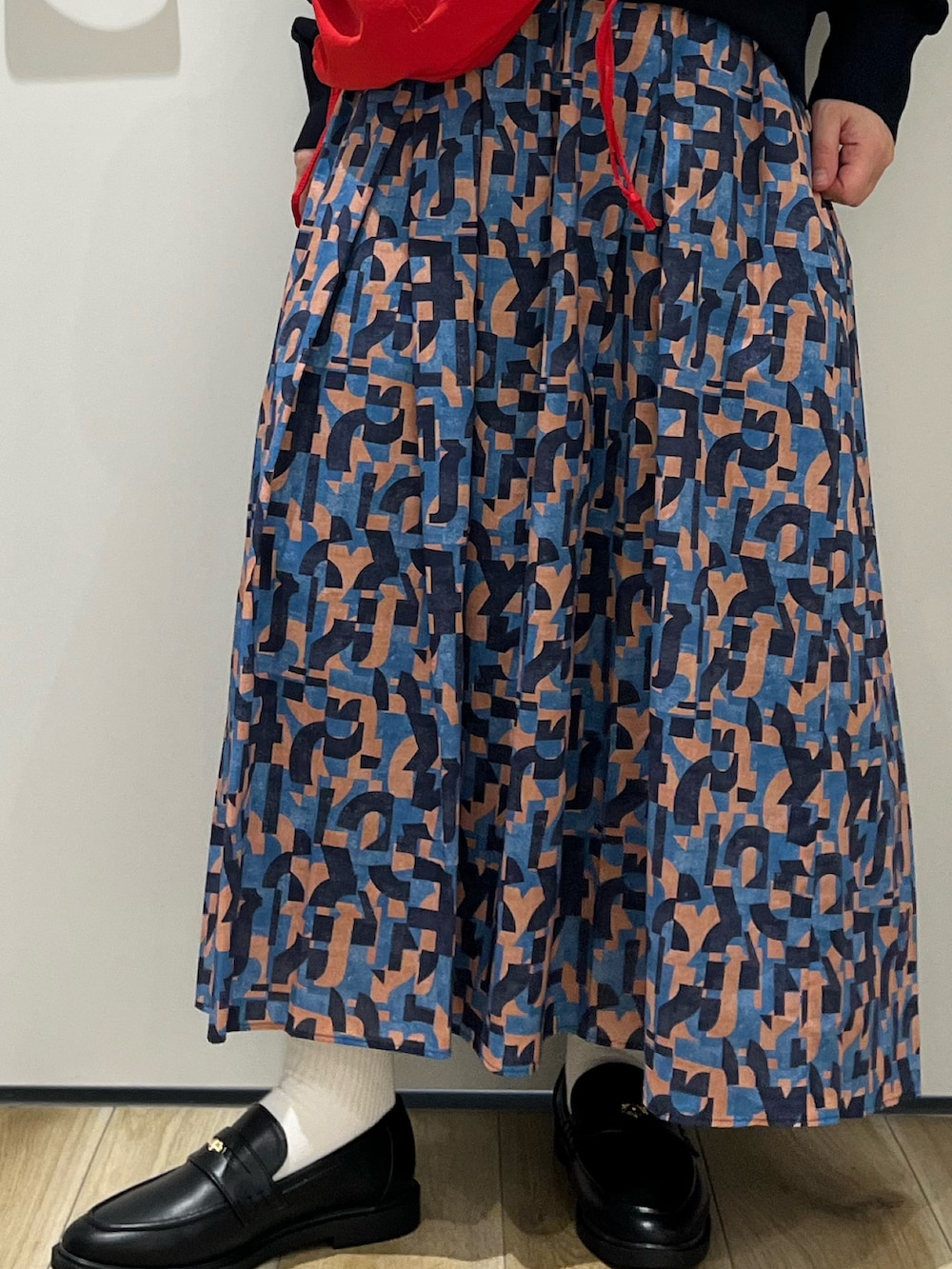 ブラック系のローファー、ブルー系のスカート、レッド系のショルダーバッグを着用したレディースの春コーディネートの6枚目の写真