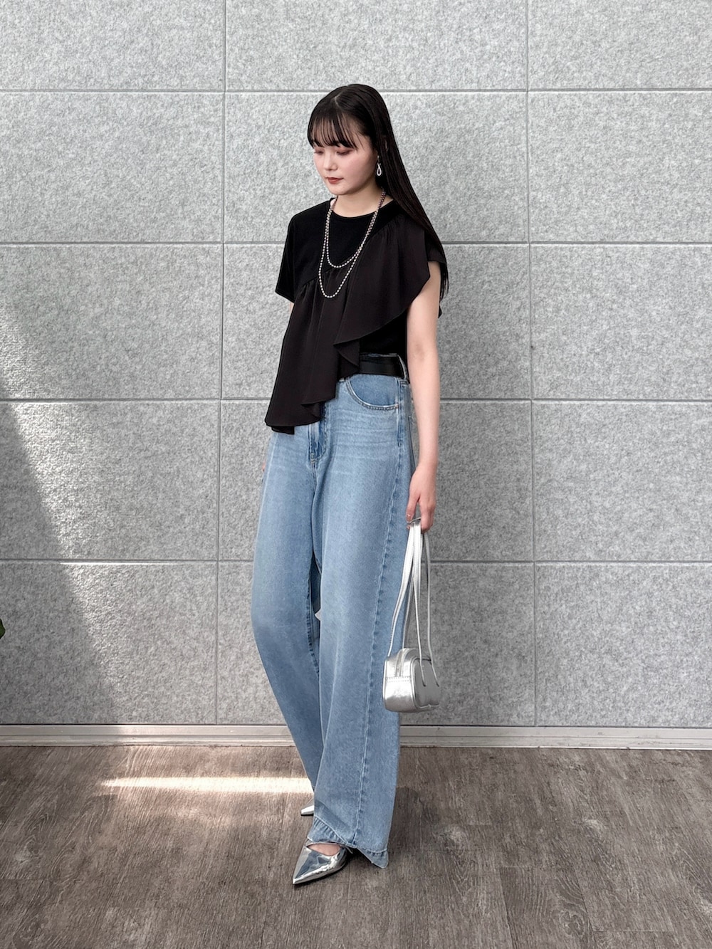 シルバー系のハンドバッグ、ブラック系のTシャツ/カットソー、ブルー系のデニムパンツを着用したレディースの夏コーディネートの2枚目の写真