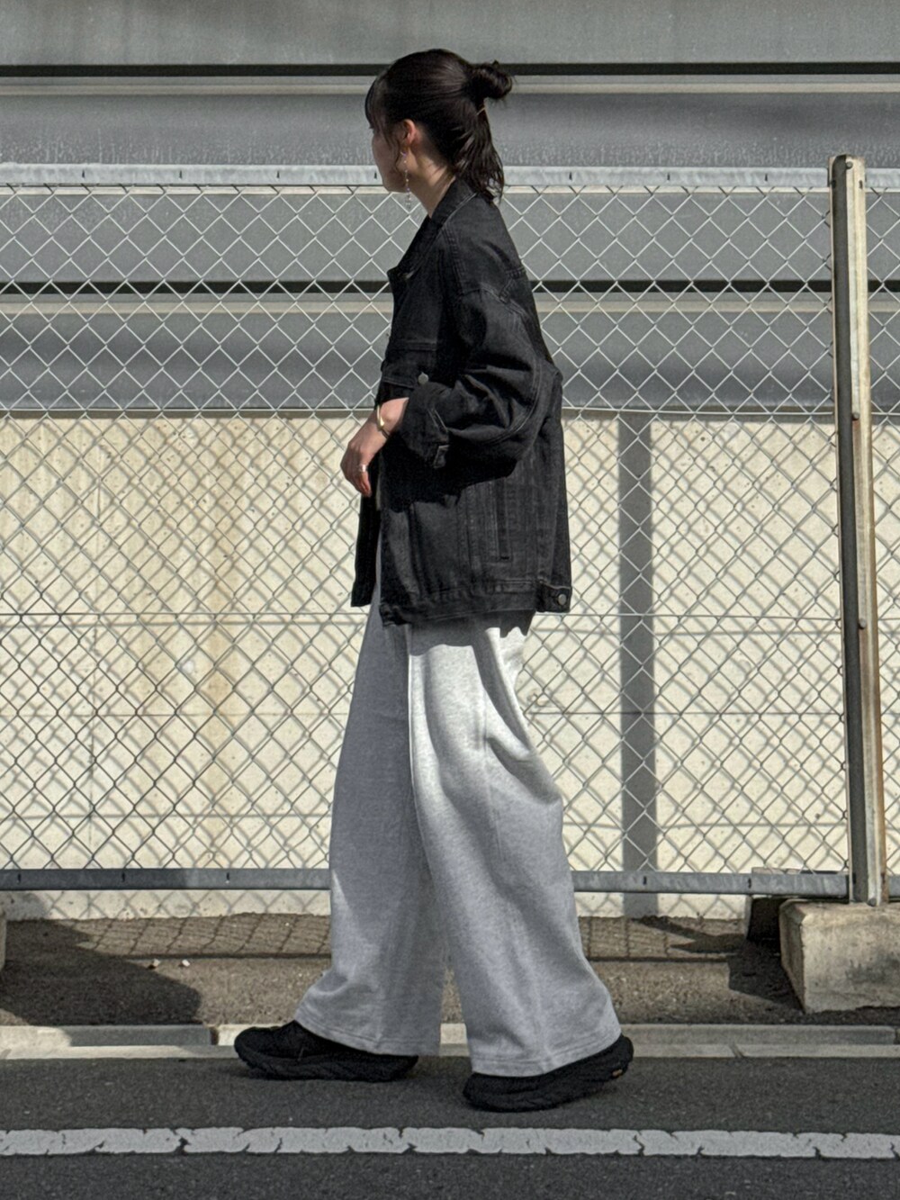ブラック系のデニムジャケット、グレー系のスウェットパンツ、ブラック系のスニーカーを着用したレディースの春コーディネートの3枚目の写真