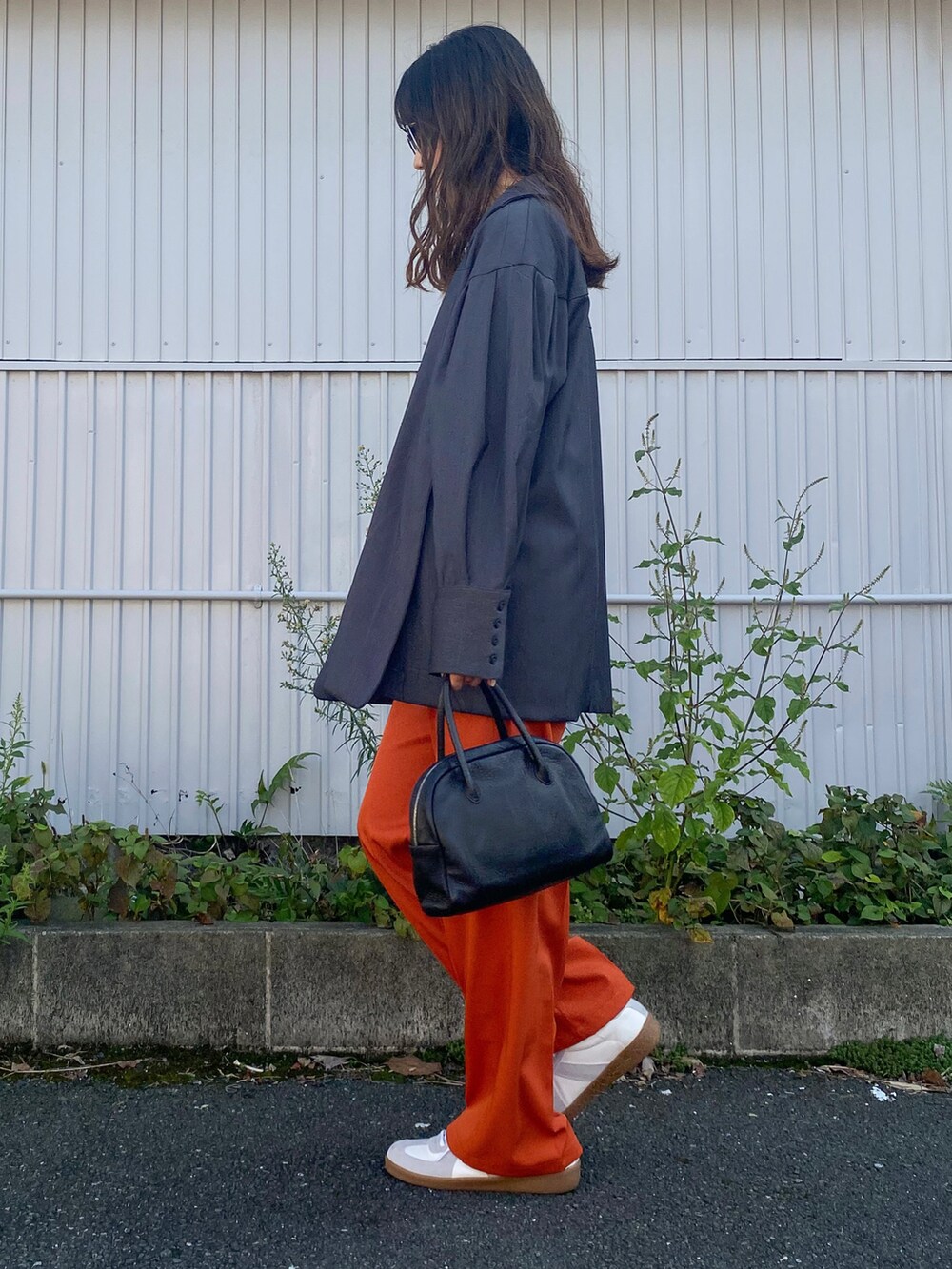 オレンジ系のスラックス、ホワイト系のTシャツ/カットソー、ブラック系のショルダーバッグを着用したレディースの秋コーディネートの2枚目の写真