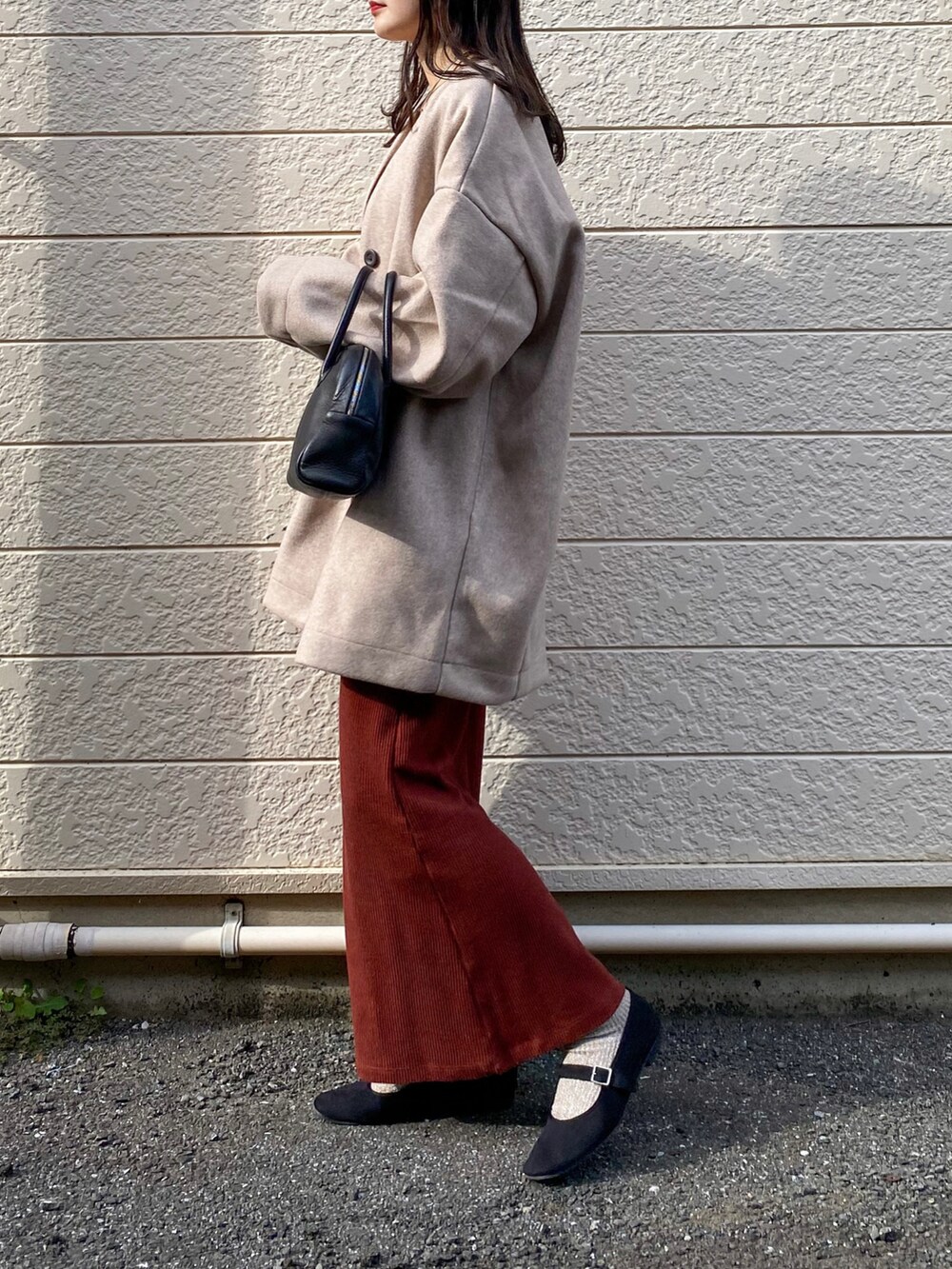 ピンク系のノーカラーコート、ブラウン系のワンピース、ブラック系のショルダーバッグを着用したレディースの秋コーディネートの2枚目の写真