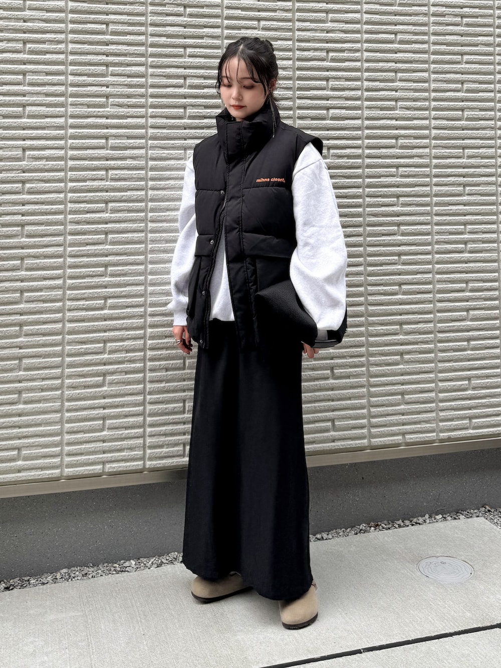 ブラック系のダウンベスト、ブラック系のスカート、ブラック系のハンドバッグを着用したレディースの秋コーディネートの3枚目の写真