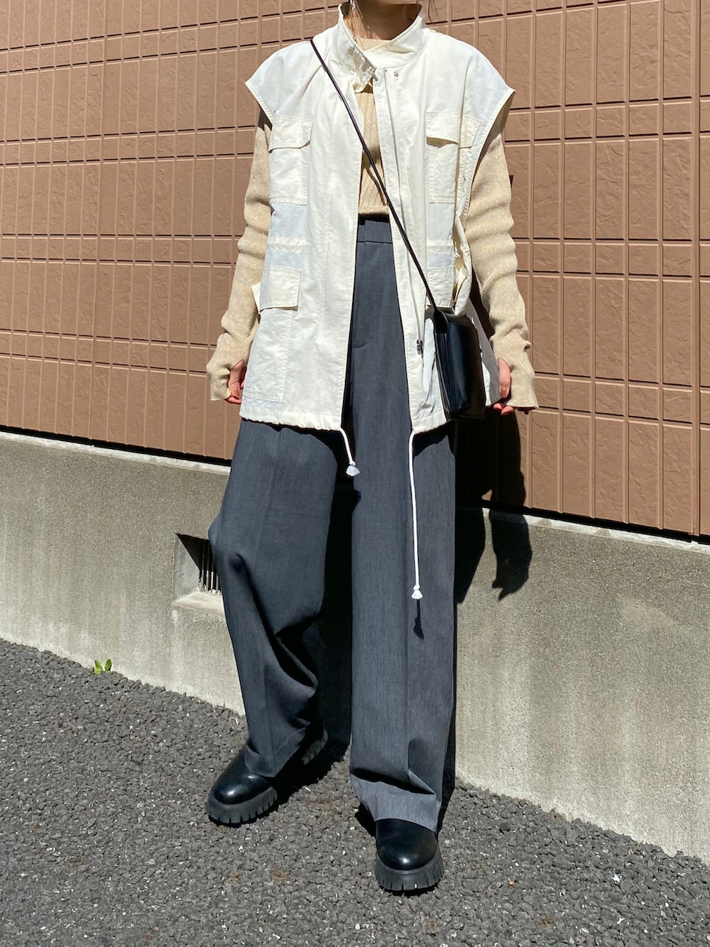 ホワイト系のベスト、グレー系のスラックス、ブラック系のショルダーバッグを着用したレディースの春コーディネートの2枚目の写真
