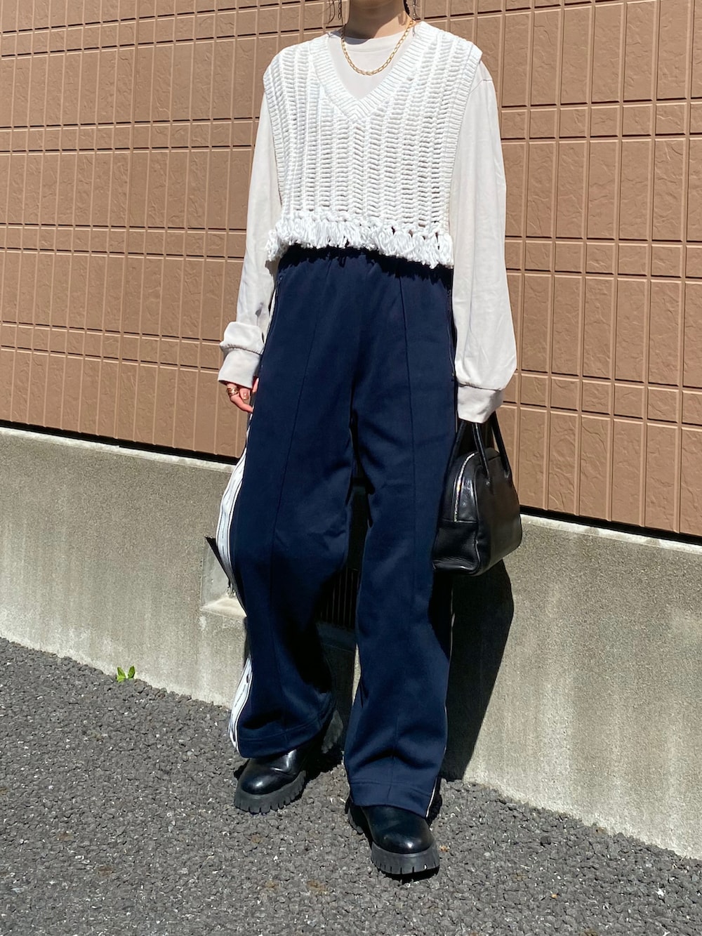 ホワイト系のベスト、ブルー系のパンツ、ブラック系のショルダーバッグを着用したレディースの春コーディネートの2枚目の写真