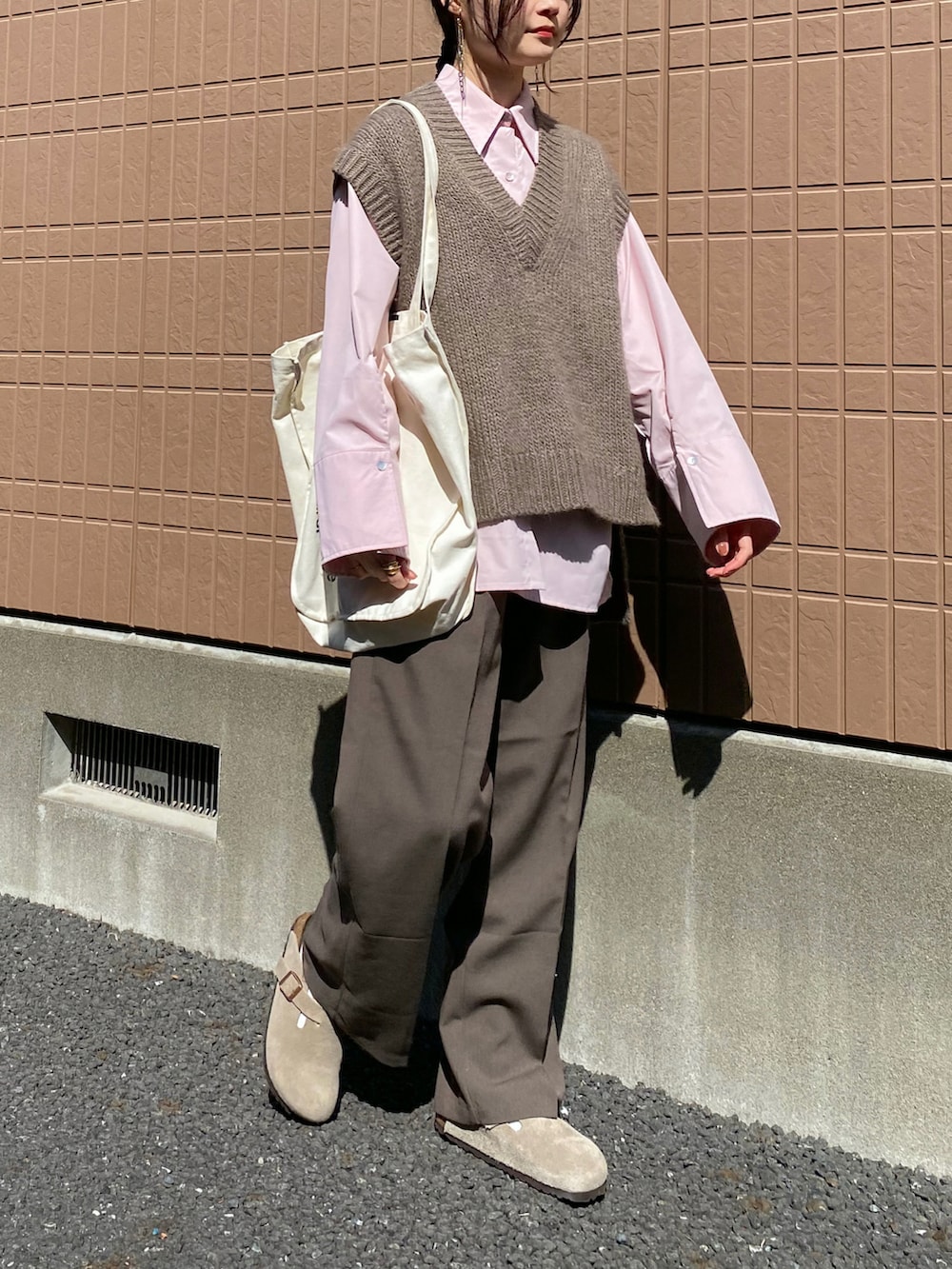 ピンク系のシャツ/ブラウス、ベージュ系のニット/セーター、ブラウン系のスラックスを着用したレディースの春コーディネートの2枚目の写真