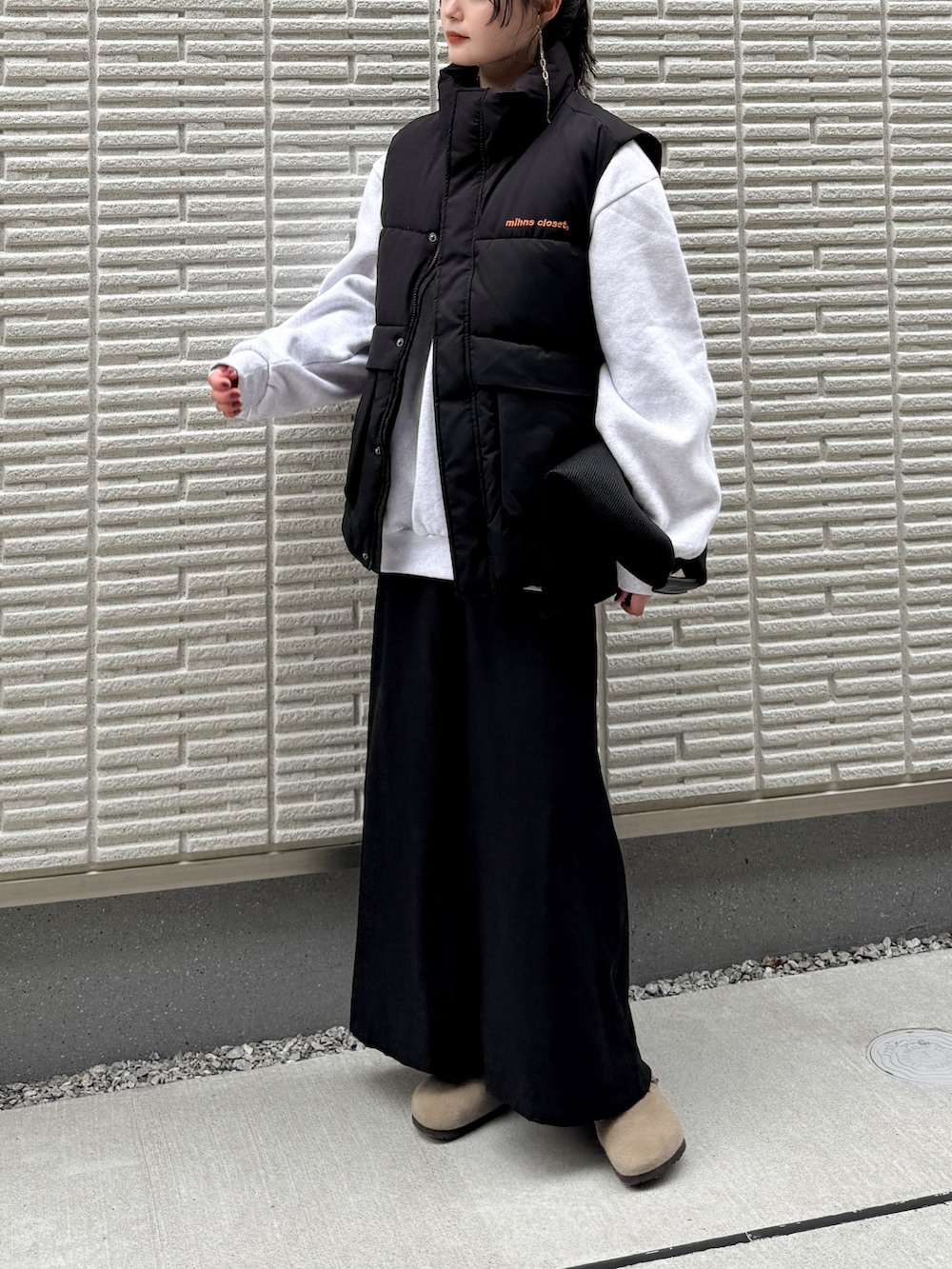 ブラック系のダウンベスト、ブラック系のスカート、ブラック系のハンドバッグを着用したレディースの秋コーディネートの2枚目の写真