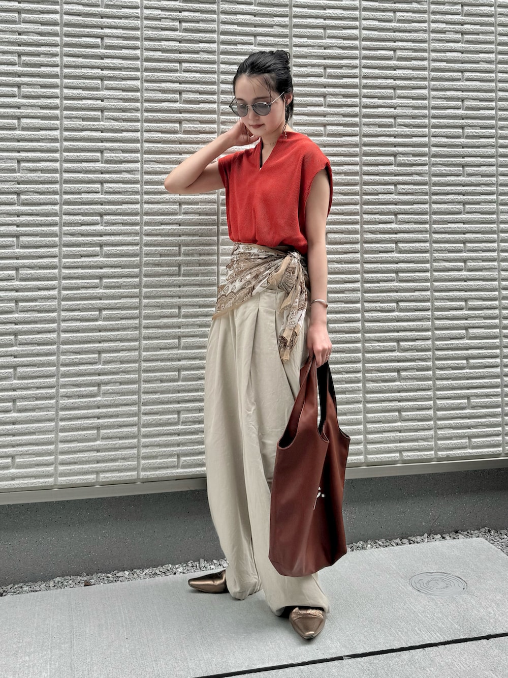 オレンジ系のTシャツ/カットソー、ベージュ系のその他パンツ、ブラウン系のトートバッグを着用したレディースの夏コーディネートの2枚目の写真