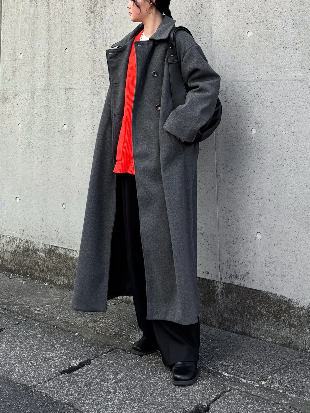 グレー系のステンカラーコート、レッド系のニット/セーター、ブラック系のその他パンツを着用したレディースの冬コーディネートの3枚目の写真