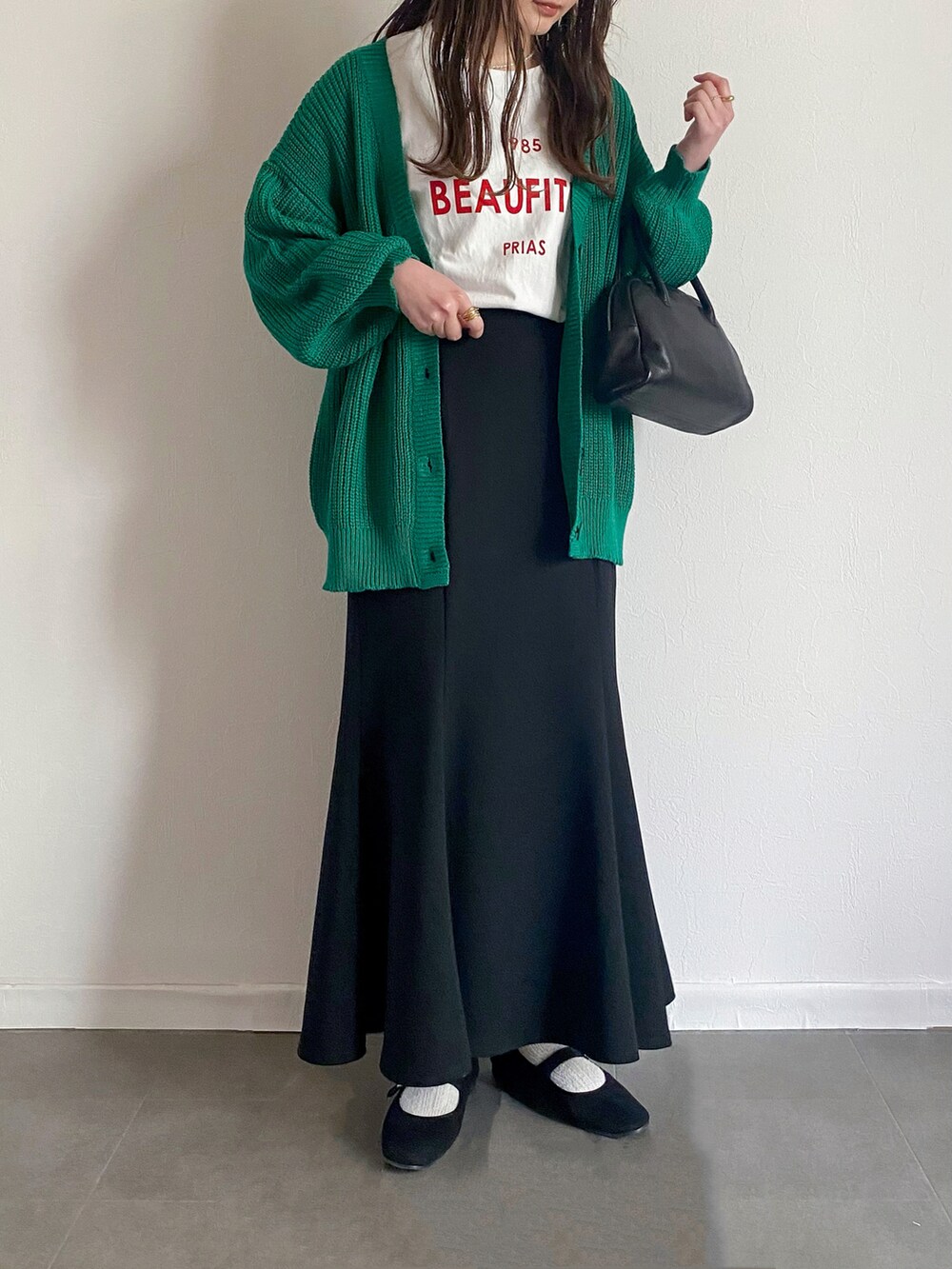 グリーン系のカーディガン/ボレロ、ホワイト系のTシャツ/カットソー、ブラック系のスカートを着用したレディースの春コーディネートの2枚目の写真