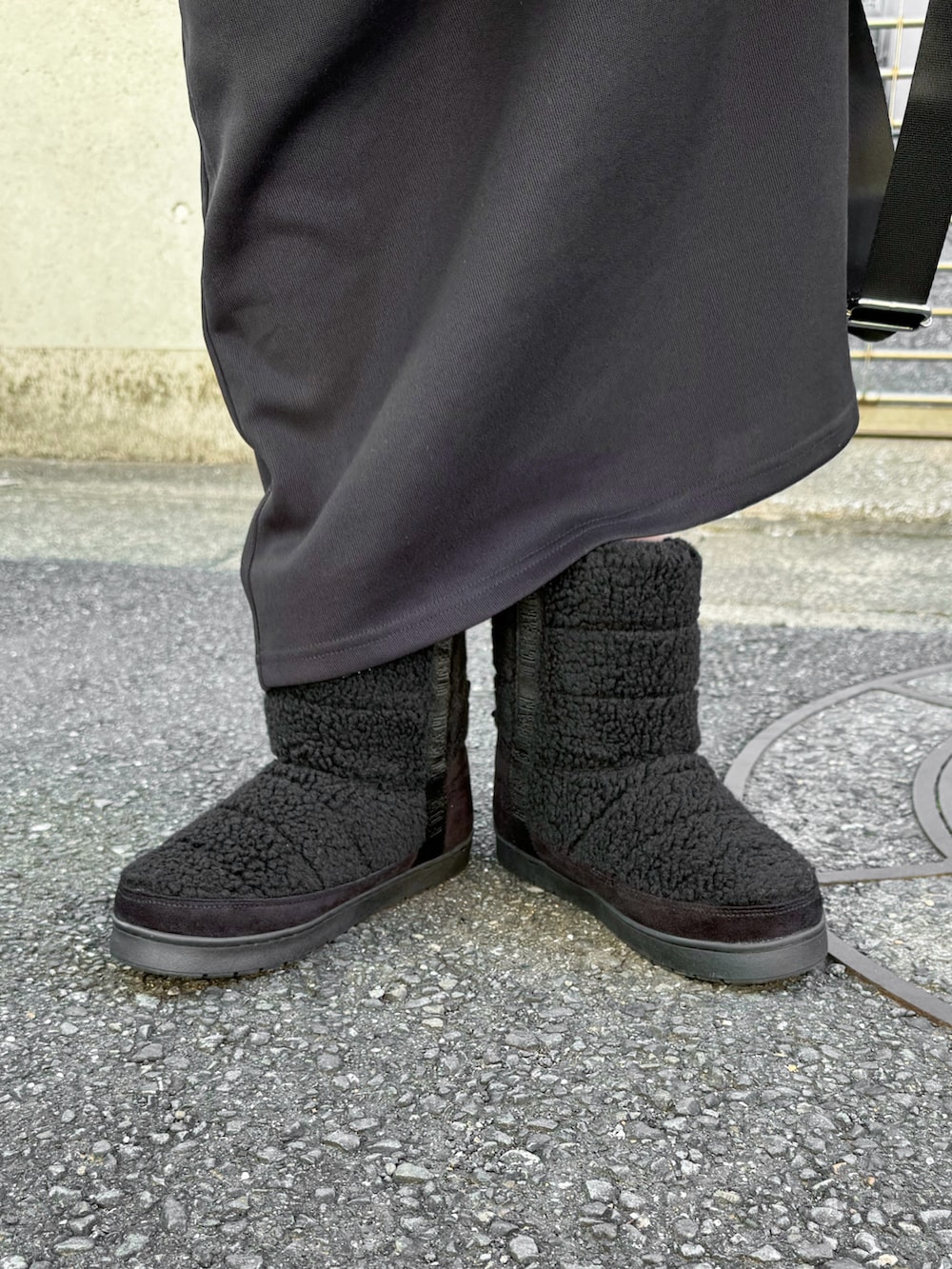 グレー系のノーカラーコート、ブラック系のブーツ、グリーン系のボストンバッグを着用したレディースの冬コーディネートの3枚目の写真