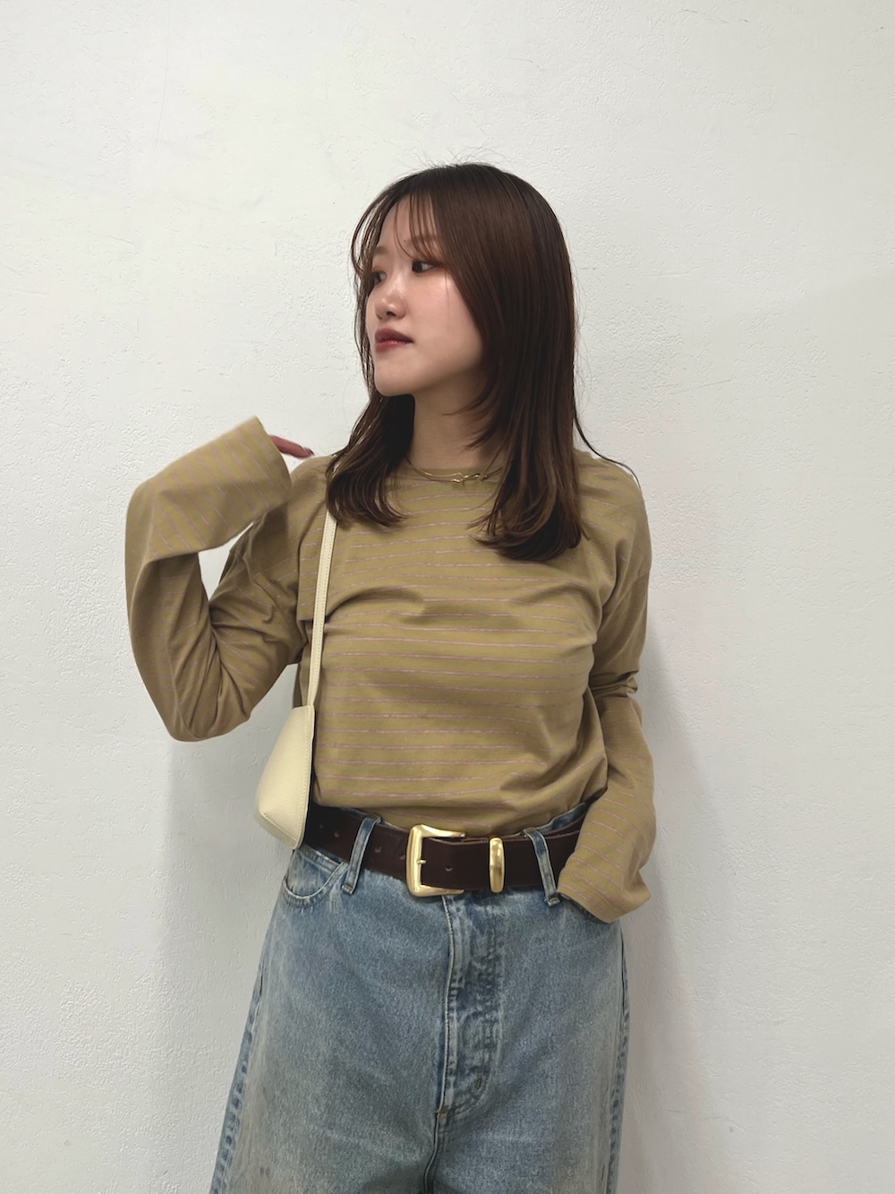 ベージュ系のTシャツ/カットソー、ブルー系のデニムパンツ、ホワイト系のショルダーバッグを着用したレディースの冬コーディネートの3枚目の写真