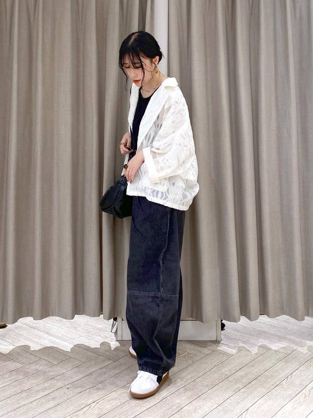 ブラック系のデニムパンツ、ホワイト系のスニーカー、ブラック系のショルダーバッグを着用したレディースの秋コーディネートの3枚目の写真