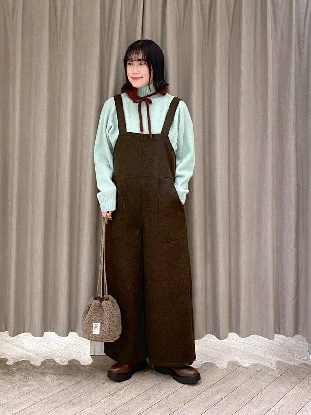 ブラウン系のブーツ、ブラウン系のハンドバッグ、グリーン系のつなぎ/オールインワンを着用したレディースの冬コーディネートの6枚目の写真