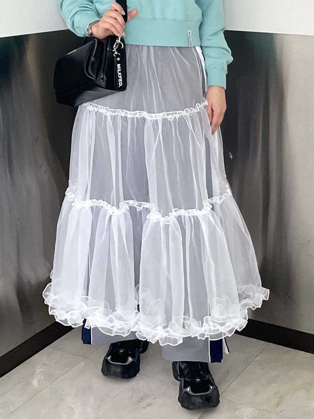 グリーン系のスウェット、ブラック系のショルダーバッグ、ホワイト系のスカートを着用したレディースの春コーディネートの5枚目の写真