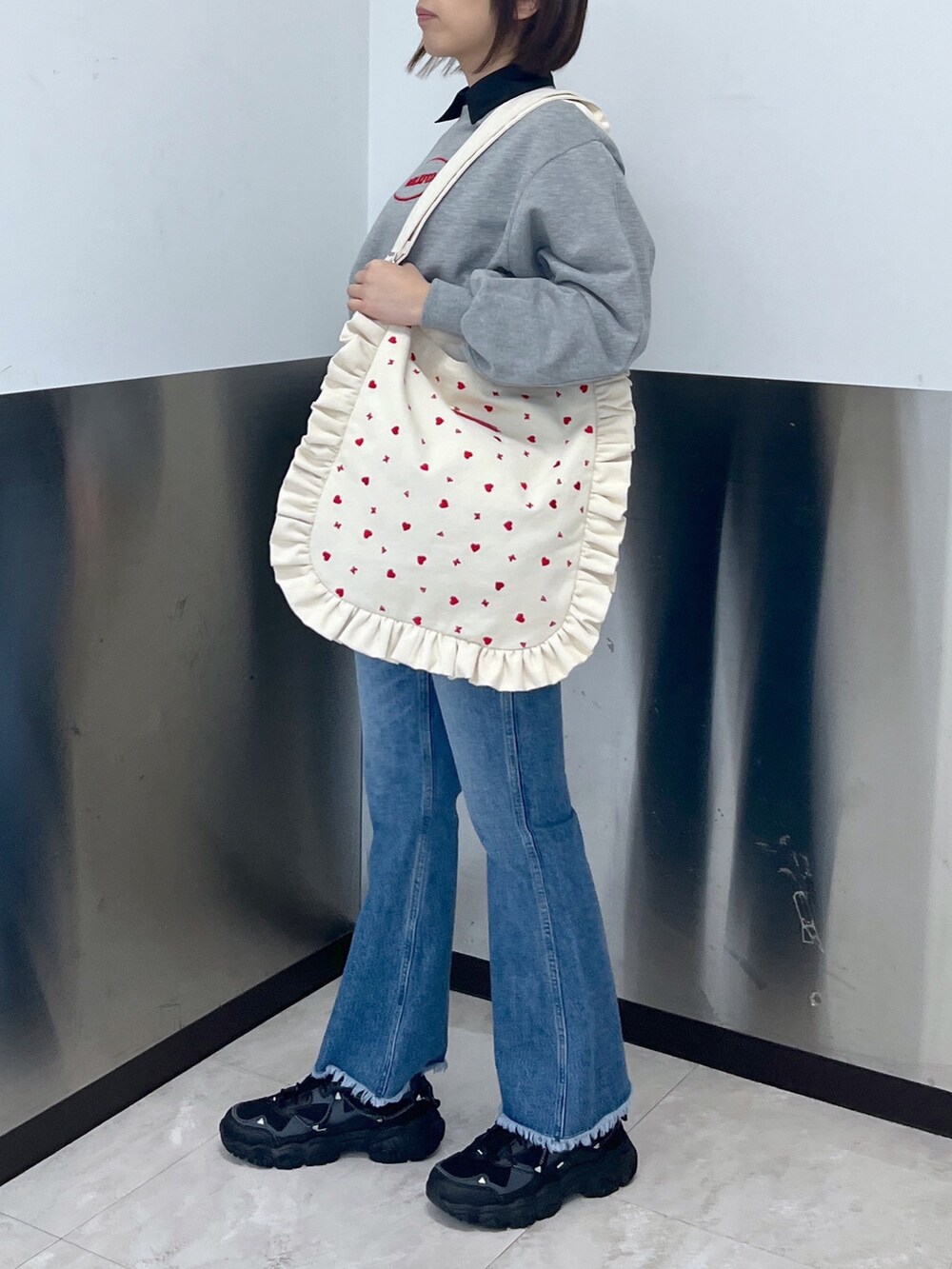 グレー系のスウェット、ブルー系のデニムパンツ、ホワイト系のショルダーバッグを着用したレディースの冬コーディネートの2枚目の写真