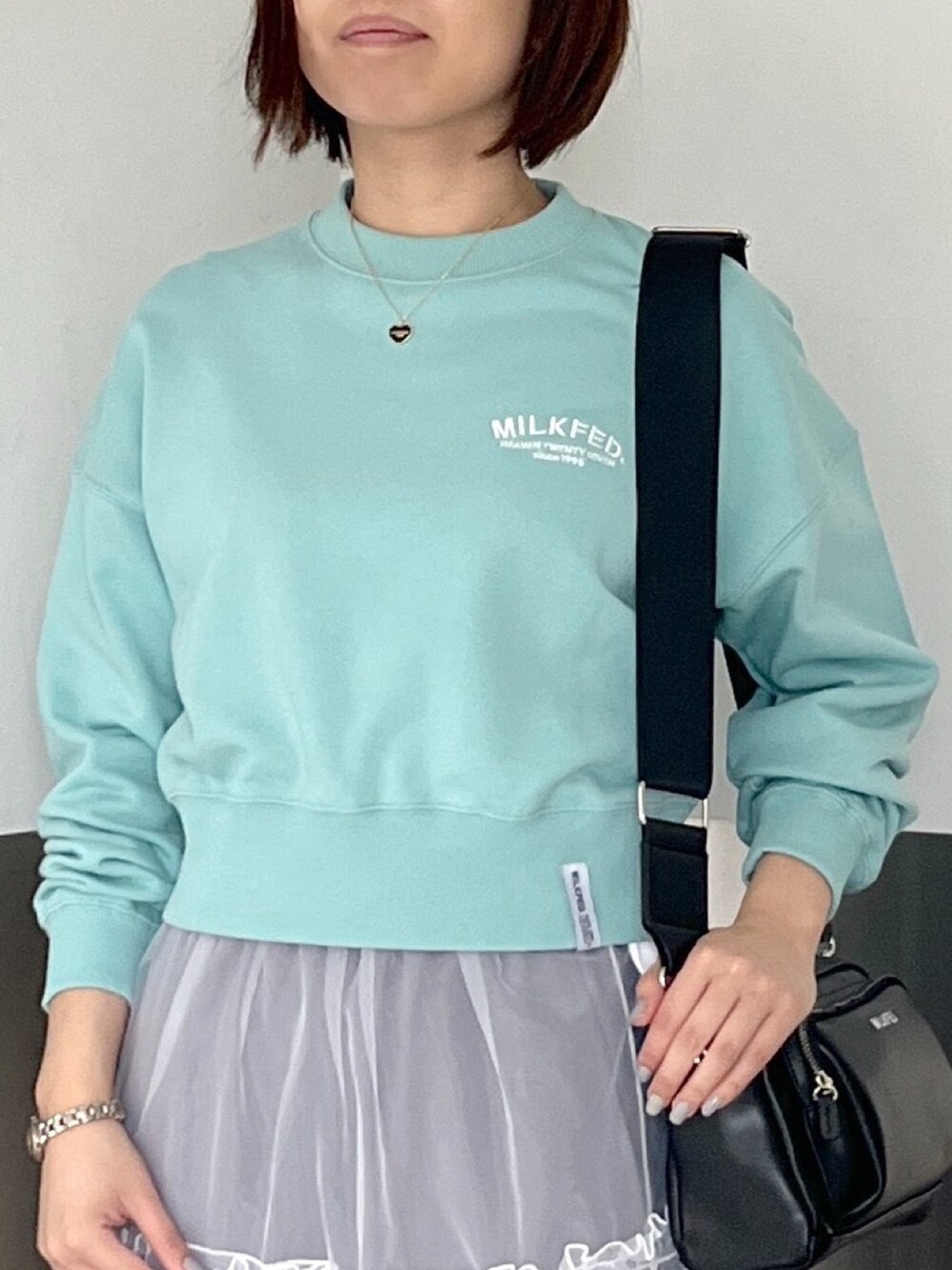 グリーン系のスウェット、ブラック系のショルダーバッグ、ホワイト系のスカートを着用したレディースの春コーディネートの4枚目の写真