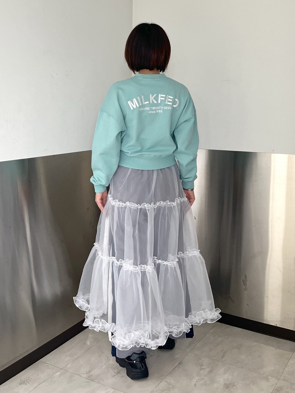 グリーン系のスウェット、ブラック系のショルダーバッグ、ホワイト系のスカートを着用したレディースの春コーディネートの3枚目の写真