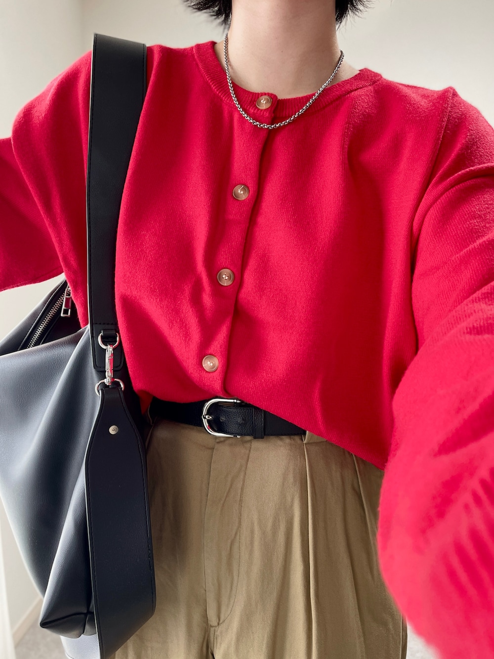 レッド系のカーディガン/ボレロ、ブラック系のショルダーバッグ、ベージュ系のチノパンツを着用したレディースの秋コーディネートの3枚目の写真