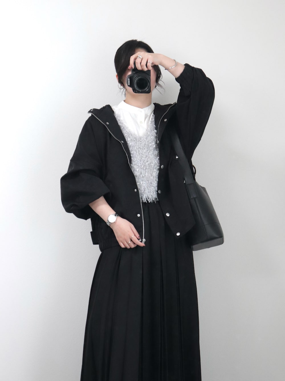 グレー系のベスト、ホワイト系のシャツ/ブラウス、ブラック系のマウンテンパーカーを着用したレディースの春コーディネートの2枚目の写真