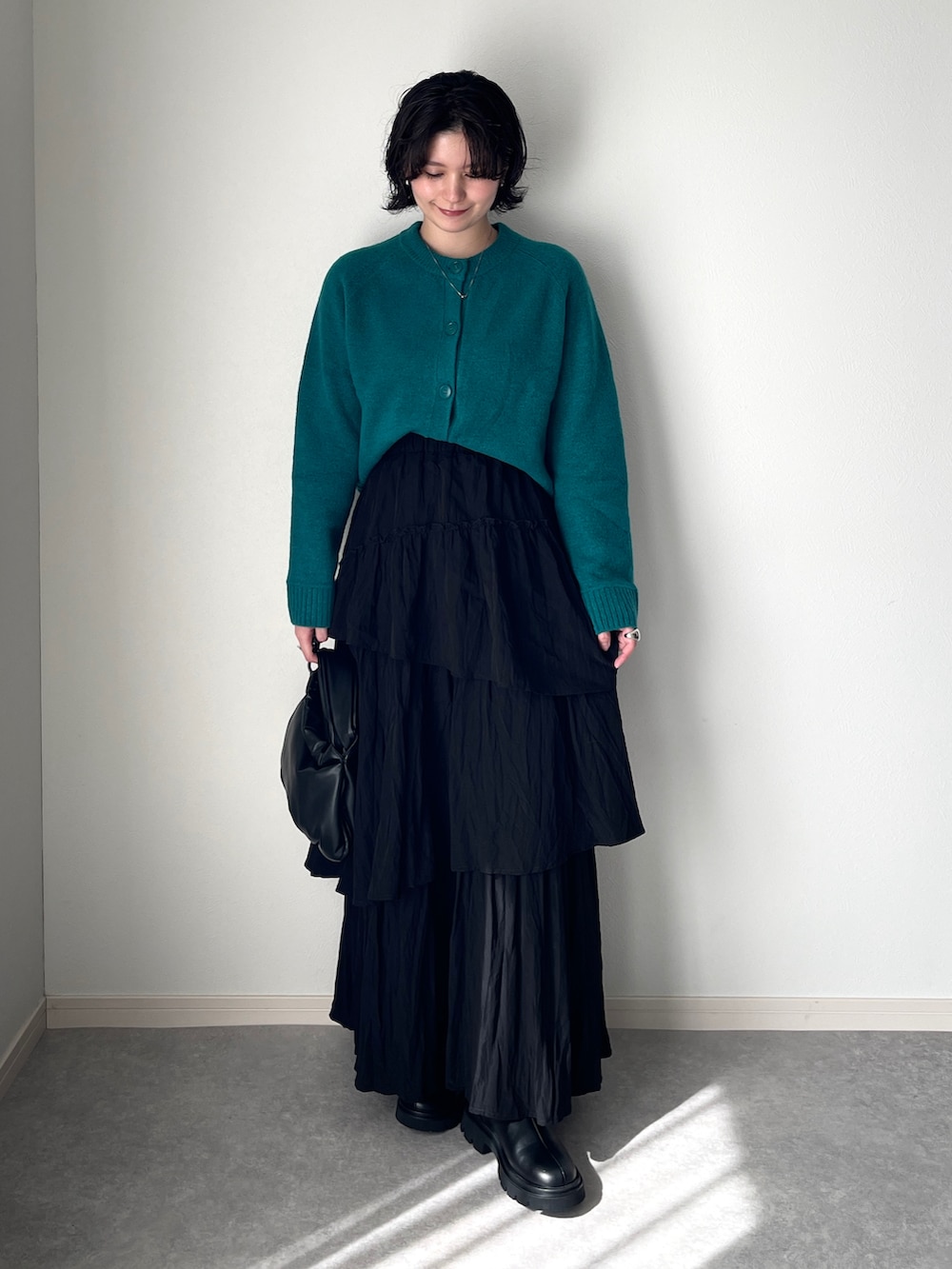 ブラック系のスカート、グリーン系のカーディガン/ボレロ、ブラック系のハンドバッグを着用したレディースの秋コーディネートの2枚目の写真