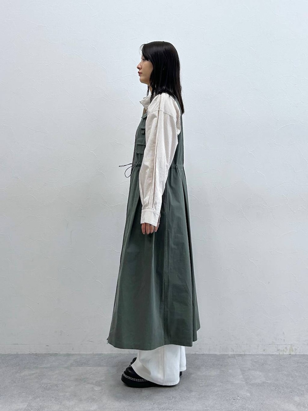 ブラック系のローファー、ホワイト系のデニムパンツ、グリーン系のジャンパースカートを着用したレディースの春コーディネートの4枚目の写真