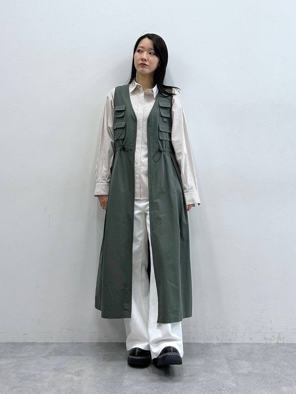 ブラック系のローファー、ホワイト系のデニムパンツ、グリーン系のジャンパースカートを着用したレディースの春コーディネートの2枚目の写真