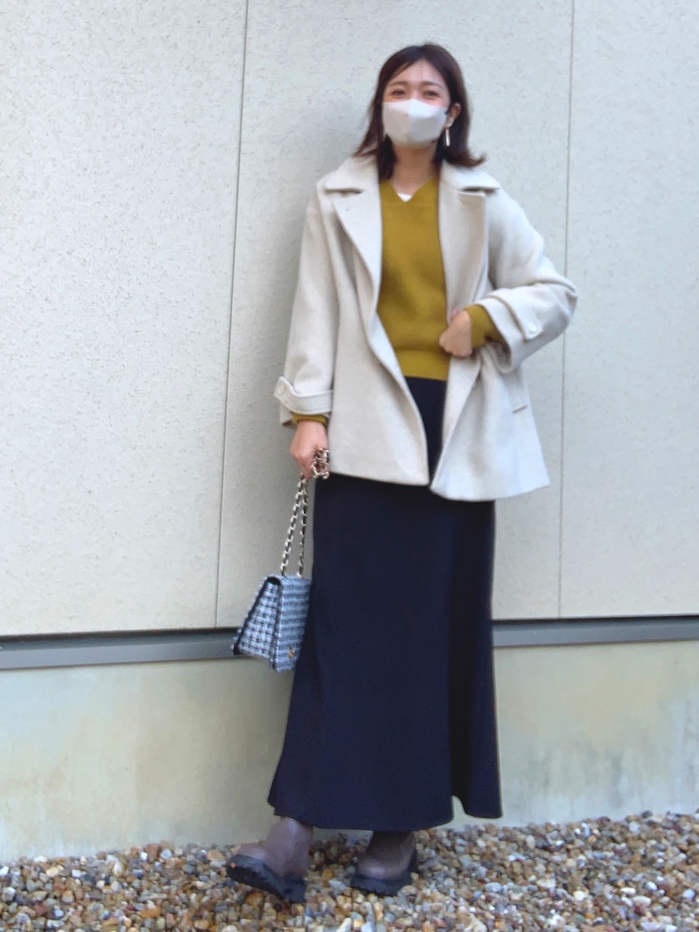 ホワイト系のジャケット/アウター、イエロー系のニット/セーター、ブラック系のスカートを着用したレディースの冬コーディネートの2枚目の写真