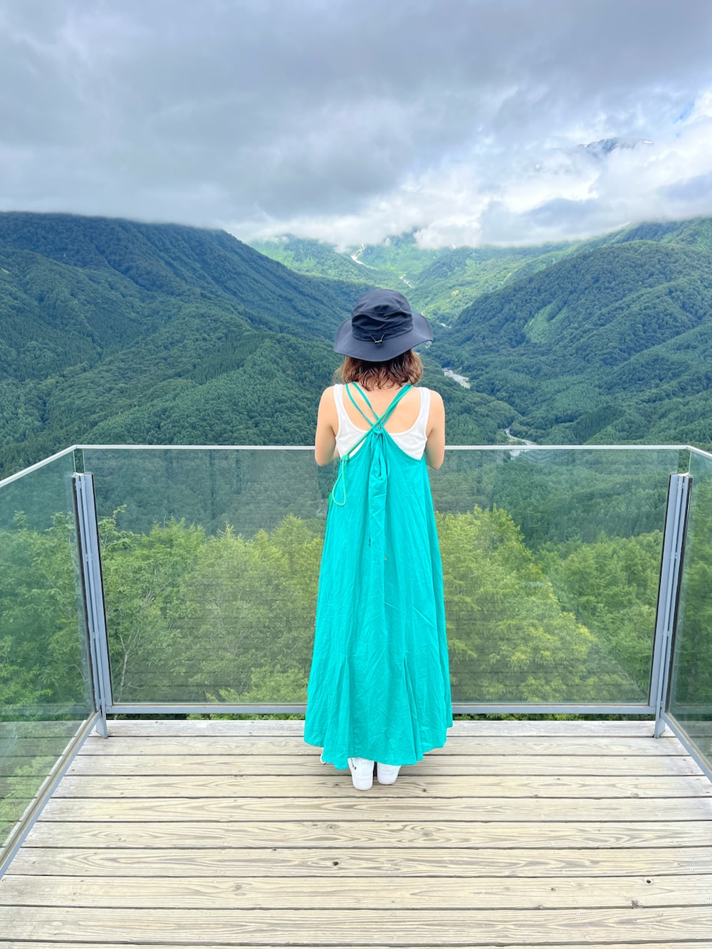 ブルー系のワンピース、ホワイト系のスニーカー、ブラック系のハットを着用したレディースの春コーディネートの2枚目の写真